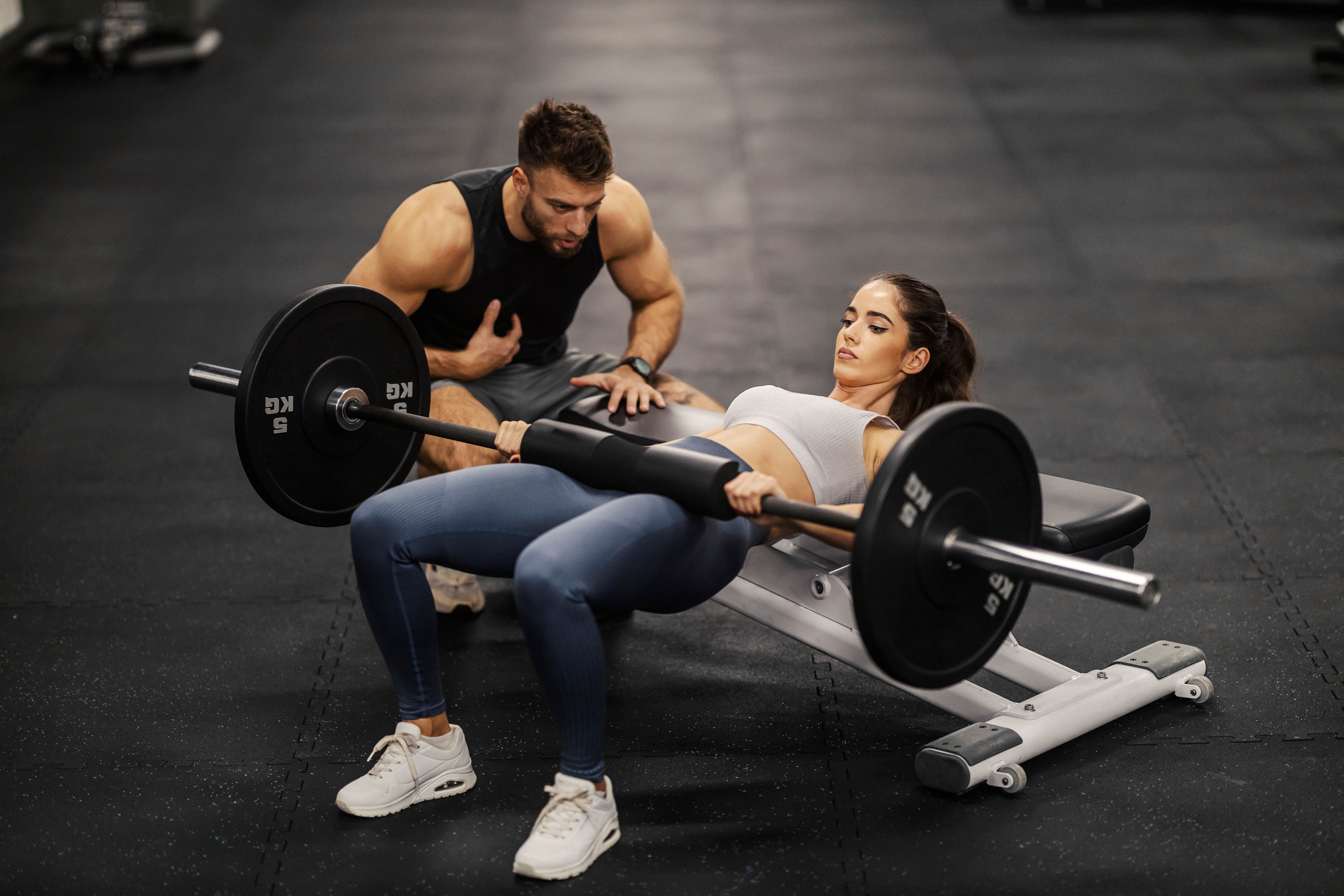 Young female client and male personal trainer doing a hip thruster in the middle of a gym